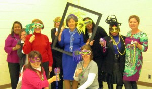 Getting in the spirit of Mardi Gras with masks are board members (kneeling) Michelle Hummer and Amy Van Riper and (standing) Linda Via, Janie Fogg, Atty Allred, Laurie Marks, K.C. Bertling, Bonita Owens, Sara Ballard and Olga Hansen. (CONTRIBUTED)