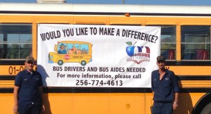 Two transportation employees tied a banner on a Madison City Schools bus to advertise the openings for bus driver. (CONTRIBUTED) 