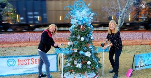 As a train rumbles by, Karen Denzine, at left, and Mary Howard with JustServe decorate the organization's Christmas tree on Main Street. RECORD PHOTOS/RANDY COX 